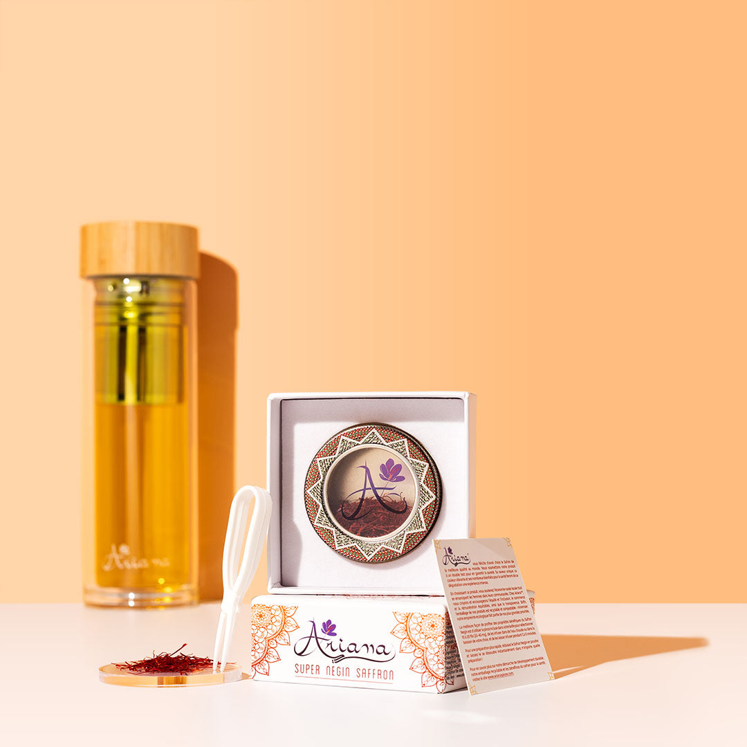 Ariana Naturals Pure 1 gram saffron packaging with a bottle infuser, tweezers, and a pile of saffron on a glass dish, on white surface and an orange background