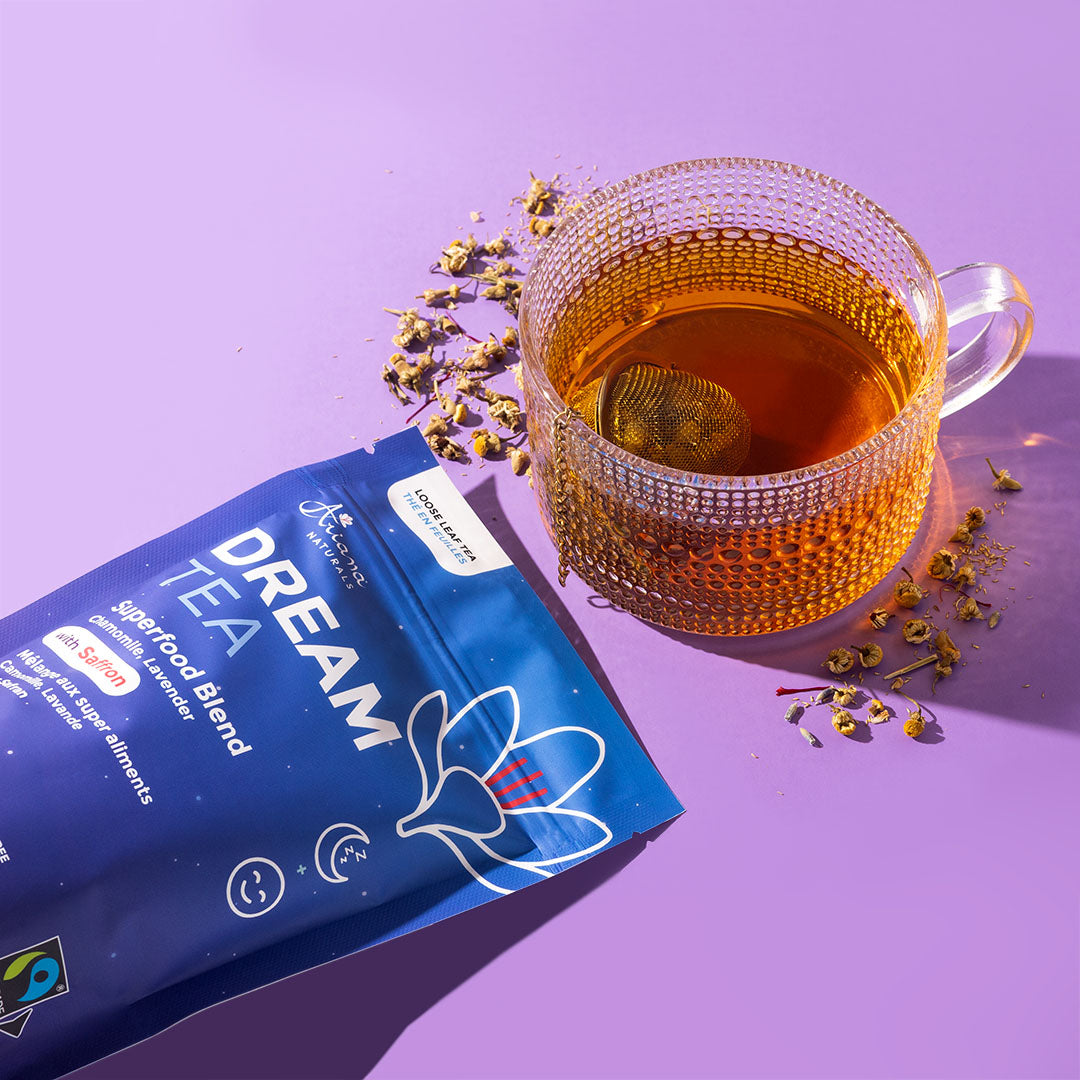 Ariana Naturals Dream Tea packaging with a cup of the tea and it's ingredients, chamomile, lavender, and saffron spilling around the tea cup on a purple background