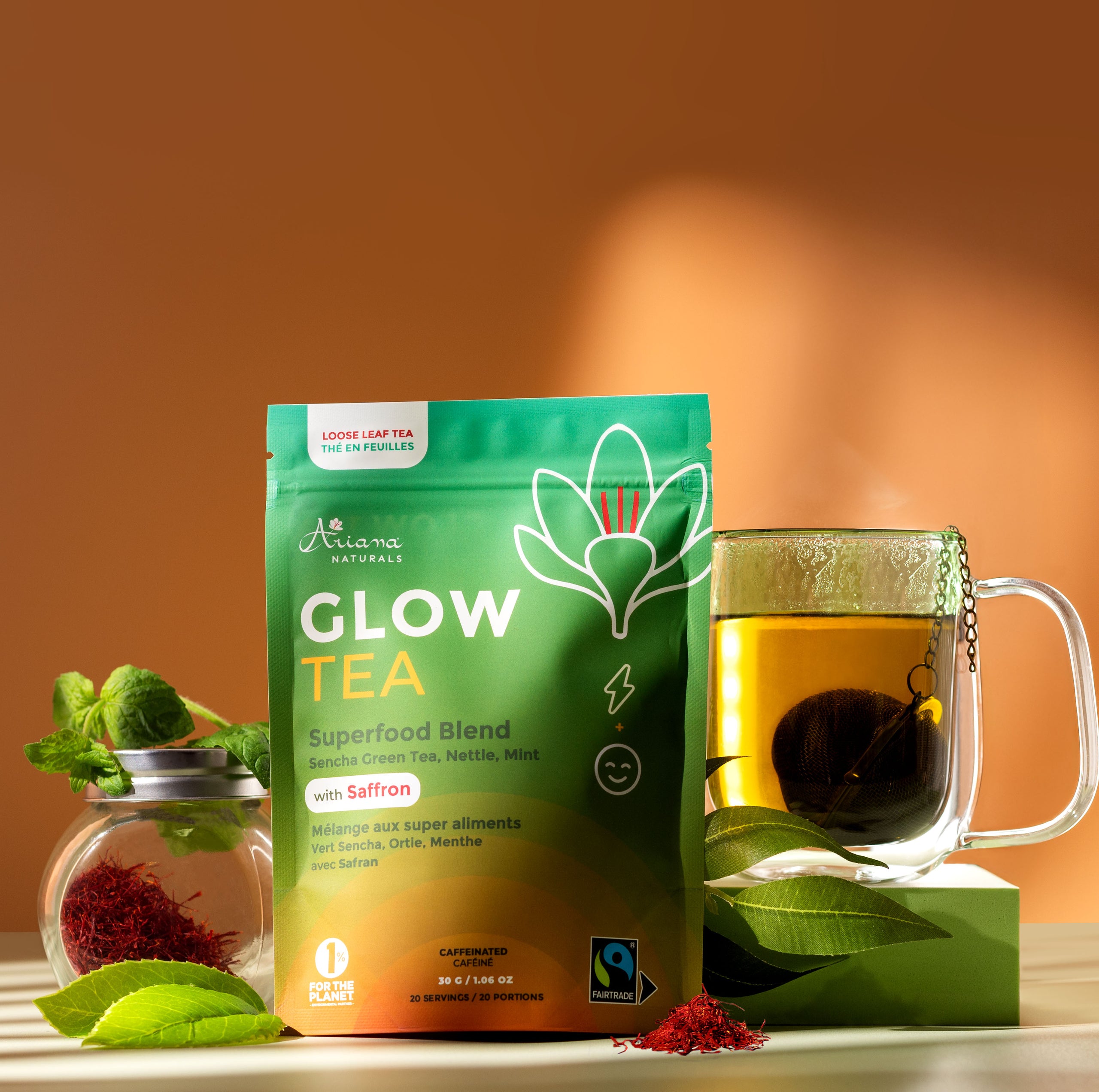 Ariana Naturals Glow Tea package with a glass mug of tea and tea ingredients, Sencha Green Tea, Nettle, Mint, and Saffron on a orange and light green background.